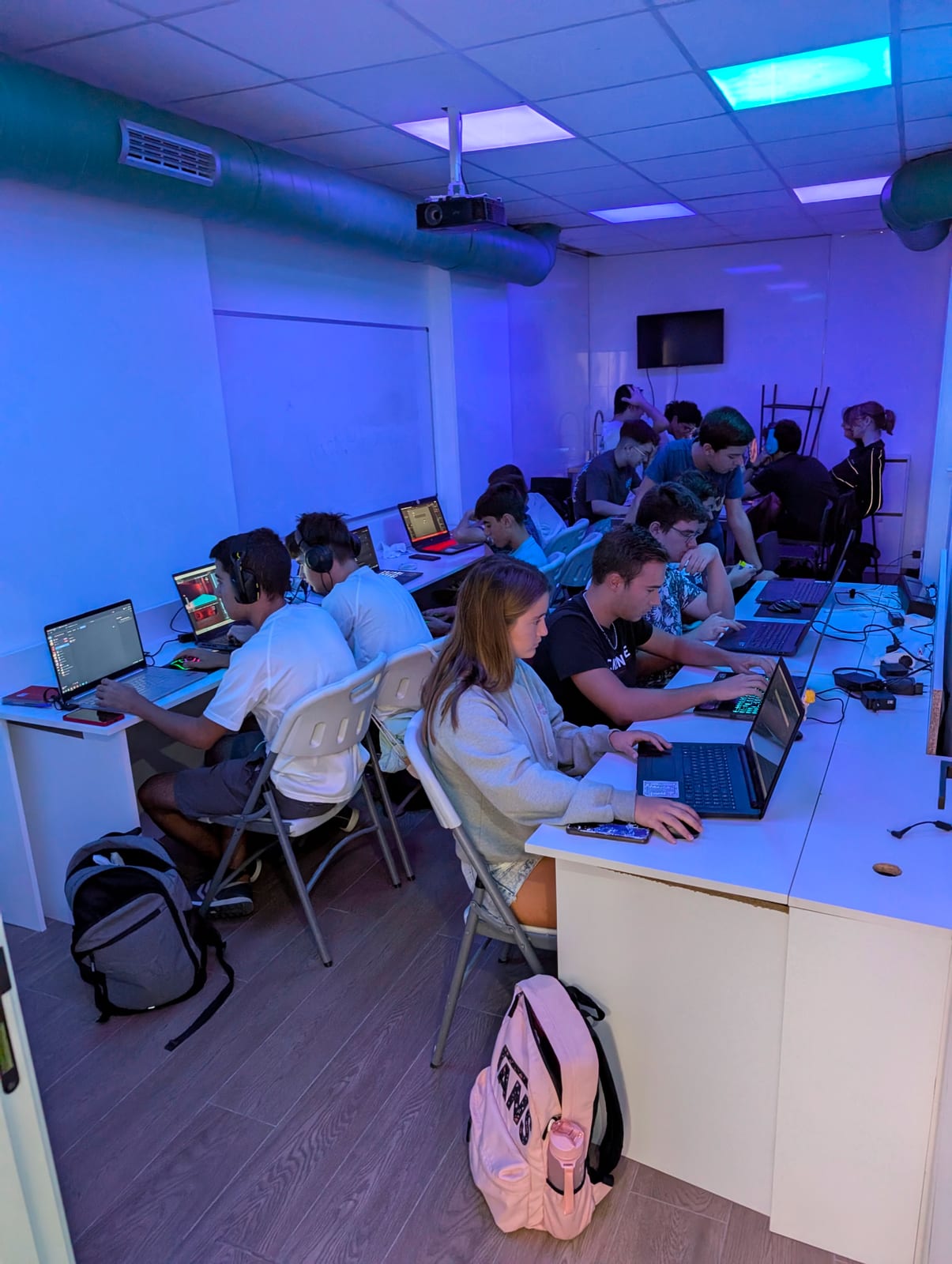 Students code on laptops under blue lighting during the Daydream Valencia game jam.
