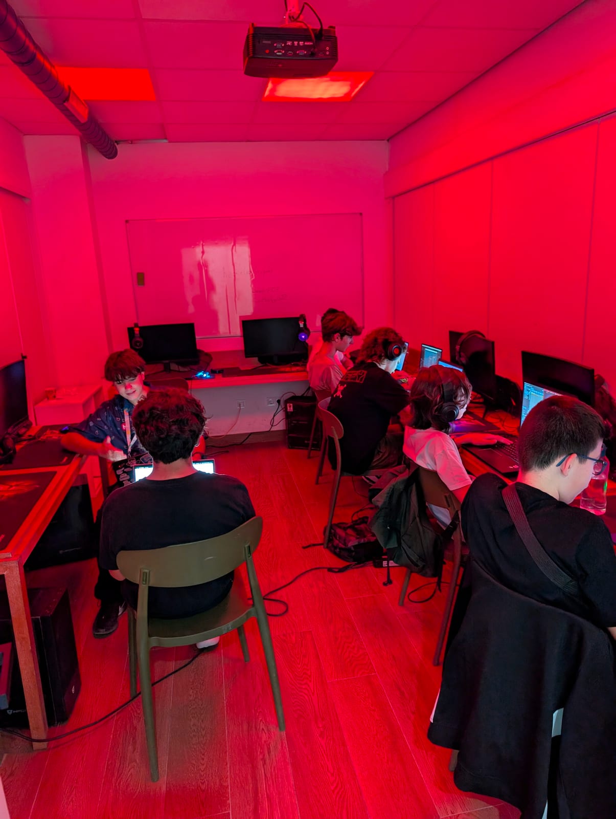 Students code on their laptops and chat in a red-lit room during Daydream Valencia.